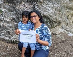 Earth Day photo petition by CCN Member in Trinidad & Tobago. A young woman and boy are holding a sign which reads 'Adapt Now to Save Lives'.